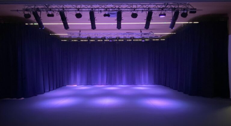 Image of a black box theatre with the stage lit up in purple lights